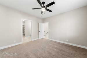 Unfurnished bedroom featuring a walk in closet, ceiling fan, a closet, and light colored carpet