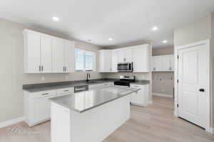 Kitchen featuring appliances with stainless steel finishes, light wood-type flooring, sink, a center island, and white cabinetry