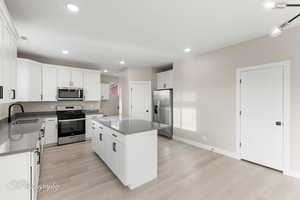 Kitchen featuring a center island, white cabinets, sink, light wood-type flooring, and stainless steel appliances