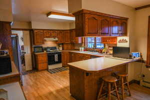 Kitchen featuring kitchen peninsula, sink, white range with gas stovetop, and light hardwood / wood-style flooring