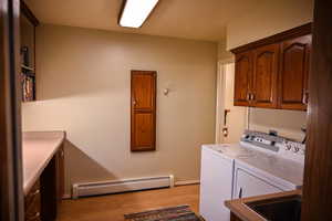 Laundry room featuring washing machine and clothes dryer, sink, cabinets, baseboard heating, and light hardwood / wood-style flooring