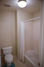 Bathroom with shower / tub combo with curtain, a textured ceiling, and toilet