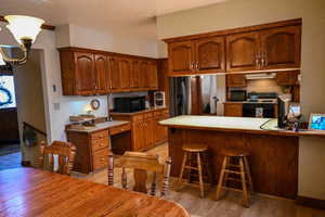 Kitchen with kitchen peninsula, a kitchen breakfast bar, gas range gas stove, light hardwood / wood-style flooring, and stainless steel fridge with ice dispenser