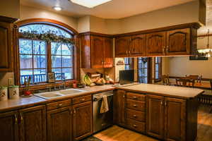 Kitchen with kitchen peninsula, light wood-type flooring, stainless steel dishwasher, and sink