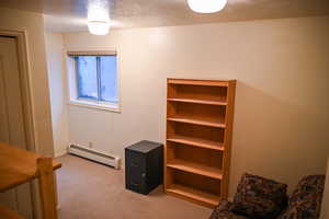 Bedroom with light carpet, a textured ceiling, and a baseboard heating unit