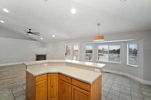 Kitchen featuring a center island, lofted ceiling, ceiling fan, decorative light fixtures, and a tiled fireplace