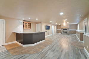 Kitchen with a stone fireplace, kitchen peninsula, wood-type flooring, and a textured ceiling