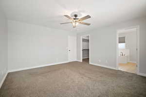 Unfurnished bedroom with ceiling fan, light colored carpet, a spacious closet, and ensuite bath