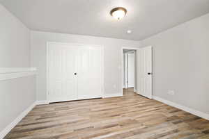 Unfurnished bedroom with a textured ceiling, light hardwood / wood-style floors, and a closet