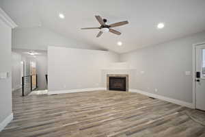 Unfurnished living room with light wood-type flooring, vaulted ceiling, ceiling fan, and a tiled fireplace