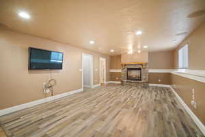 Unfurnished living room with a stone fireplace, wood-type flooring, and a textured ceiling