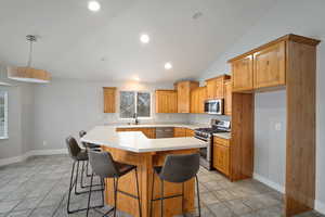 Kitchen featuring appliances with stainless steel finishes, vaulted ceiling, sink, a center island, and a breakfast bar area