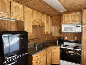 Kitchen featuring wooden walls, white appliances, sink, and wood ceiling