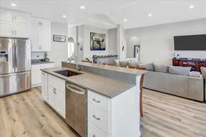 Kitchen featuring a center island with sink, white cabinets, sink, light hardwood / wood-style flooring, and stainless steel appliances