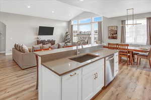 Kitchen featuring a kitchen island with sink, sink, decorative light fixtures, dishwasher, and white cabinets