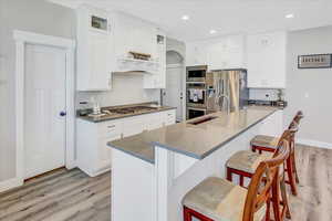 Kitchen with a kitchen bar, dark stone counters, stainless steel appliances, a center island with sink, and white cabinetry