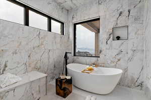 Bathroom with a mountain view, a bathing tub, a healthy amount of sunlight, and tile walls