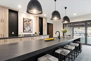 Wet bar featuring a breakfast bar area, light brown cabinetry, hanging light fixtures, and sink