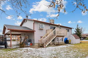 Snow covered rear of property featuring central AC unit and a storage shed