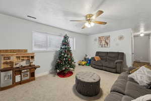 Carpeted living room with ceiling fan and a textured ceiling