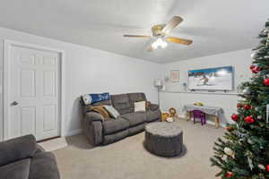 Carpeted living room featuring ceiling fan and a textured ceiling