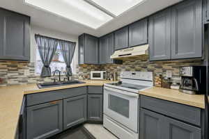 Kitchen with gray cabinetry, white appliances, sink, and tasteful backsplash