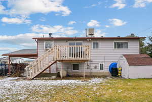 Snow covered property with a yard, a deck, a storage unit, and central air condition unit