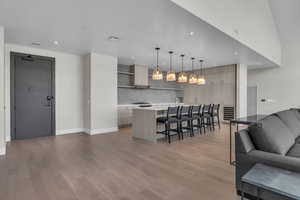 Kitchen with a breakfast bar, light brown cabinets, a center island with sink, hanging light fixtures, and light hardwood / wood-style floors