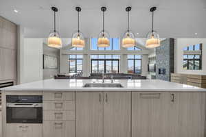 Kitchen featuring stainless steel oven, a spacious island, sink, light brown cabinetry, and decorative light fixtures