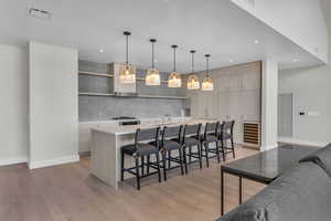 Kitchen with a kitchen bar, decorative light fixtures, light hardwood / wood-style floors, and an island with sink