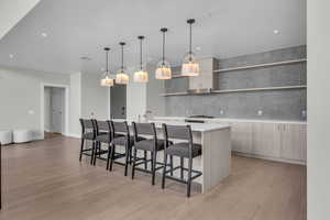 Kitchen featuring a kitchen bar, decorative light fixtures, light hardwood / wood-style flooring, and an island with sink