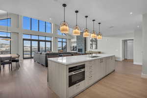 Kitchen with sink, oven, pendant lighting, a kitchen island with sink, and light wood-type flooring