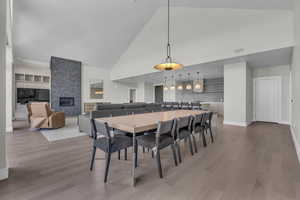 Dining space with a stone fireplace, wood-type flooring, and high vaulted ceiling