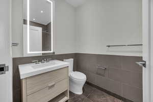 Bathroom with tile patterned flooring, vanity, toilet, and tile walls