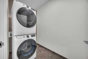 Laundry area featuring dark tile patterned floors and stacked washer and clothes dryer