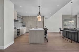 Kitchen featuring light brown cabinets, a kitchen island with sink, a kitchen bar, decorative backsplash, and appliances with stainless steel finishes