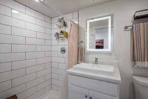 Bathroom with tiled shower, vanity, and toilet