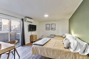 Bedroom featuring a wall mounted AC, hardwood / wood-style flooring, and access to exterior