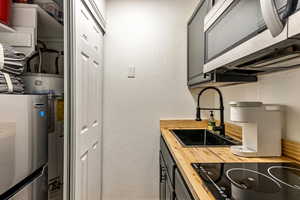 Kitchen with butcher block counters, black electric stovetop, gray cabinets, and sink