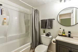 Full bathroom with vanity, toilet, shower / bathtub combination with curtain, and a textured ceiling