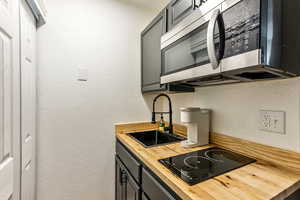 Kitchen with gray cabinetry, black electric stovetop, sink, ornamental molding, and butcher block countertops