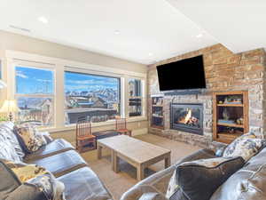 Living room with carpet flooring, built in shelves, and a stone fireplace