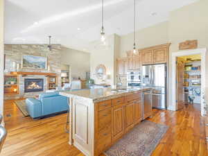 Kitchen featuring a kitchen island with sink, a kitchen breakfast bar, a fireplace, appliances with stainless steel finishes, and light stone counters