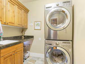 Laundry area with stacked washer and dryer, cabinets, and sink