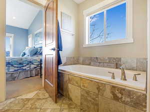 Bathroom featuring tiled bath and lofted ceiling