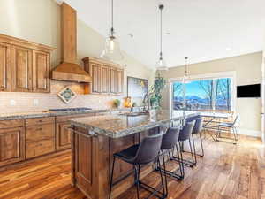 Kitchen with premium range hood, light stone counters, a breakfast bar, sink, and a center island with sink