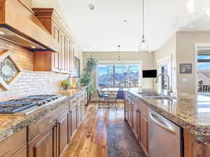 Kitchen with tasteful backsplash, custom range hood, stainless steel appliances, sink, and light hardwood / wood-style floors