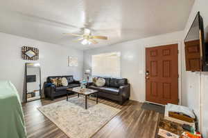 Living room with ceiling fan, dark hardwood / wood-style flooring, and a textured ceiling