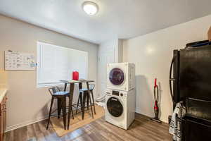 Clothes washing area featuring a textured ceiling, wood-type flooring, and stacked washer / drying machine