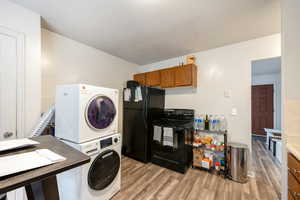 Laundry room featuring stacked washer / dryer, light hardwood / wood-style floors, and a textured ceiling